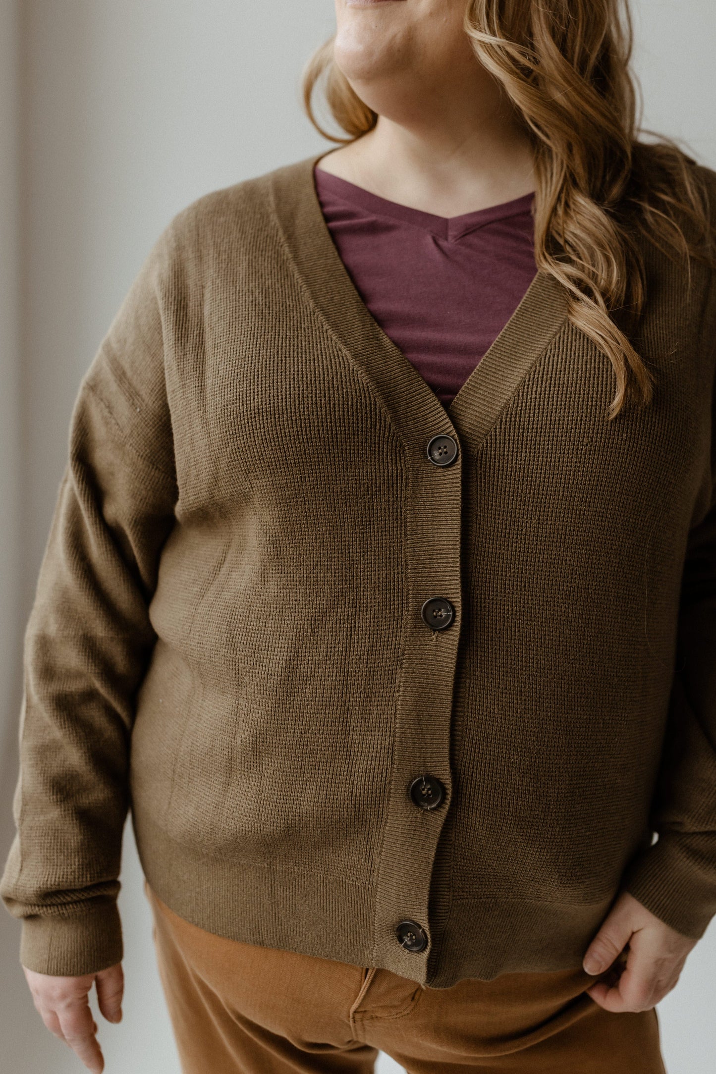 A person is wrapped in a cozy textured button front cardigan over a maroon shirt.