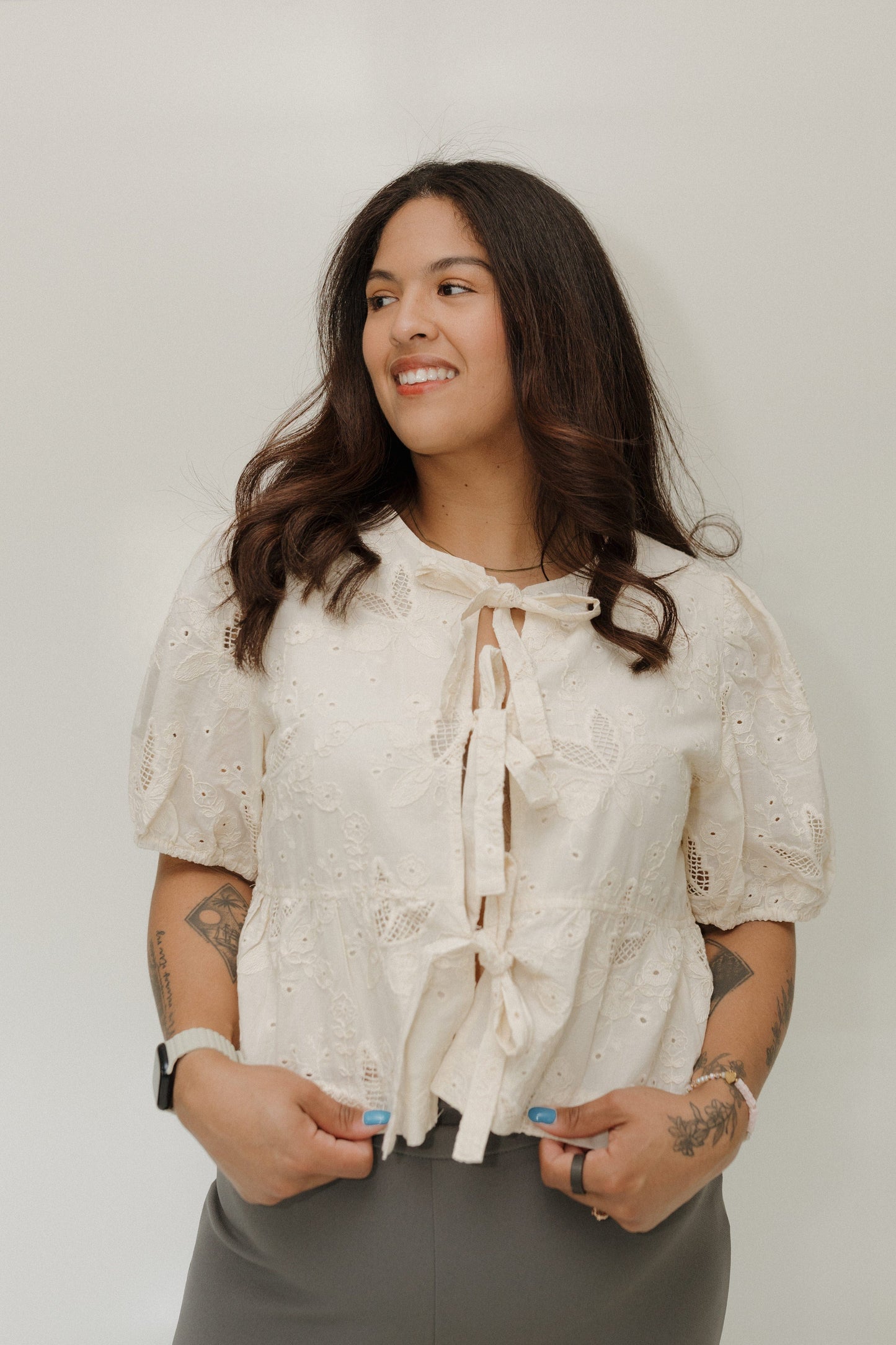 Woman wearing a white blouse with lace details against a plain background