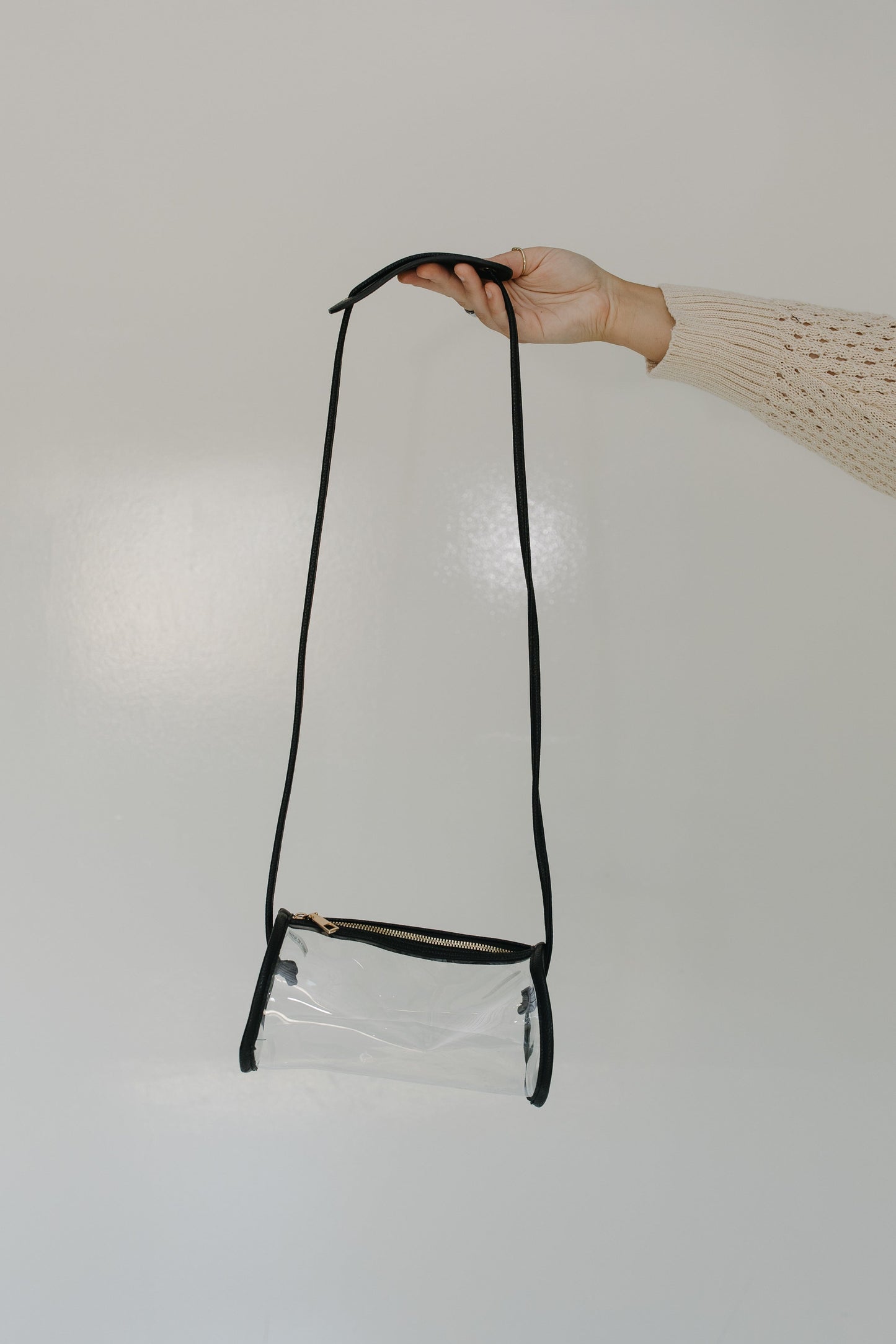 Clear crossbody bag with black strap held by a hand on a white background