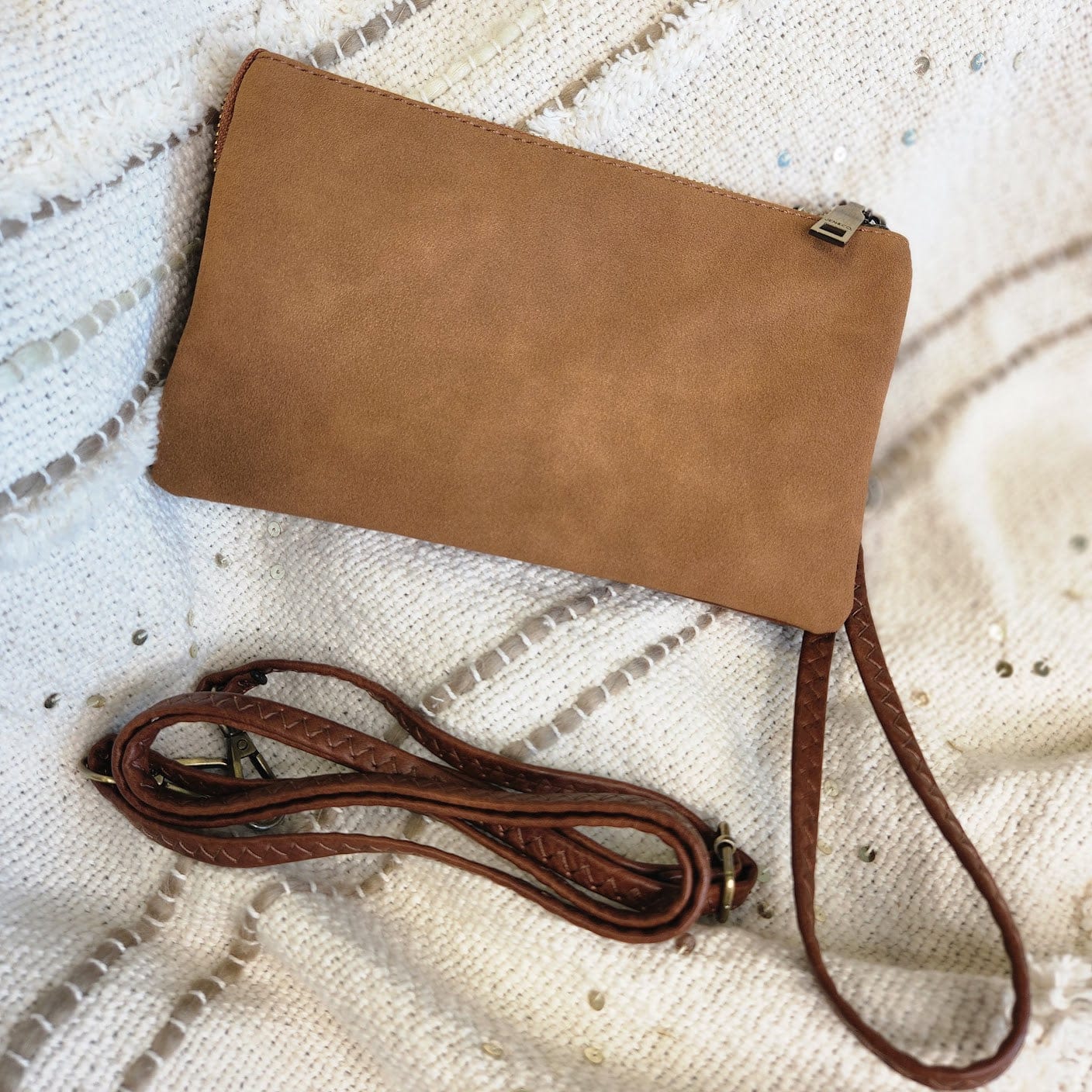 A brown leather clutch with a detachable strap is artfully displayed on a textured white fabric background, offering both elegance and versatility. Enjoy free shipping when you choose this stylish accessory for any occasion.
