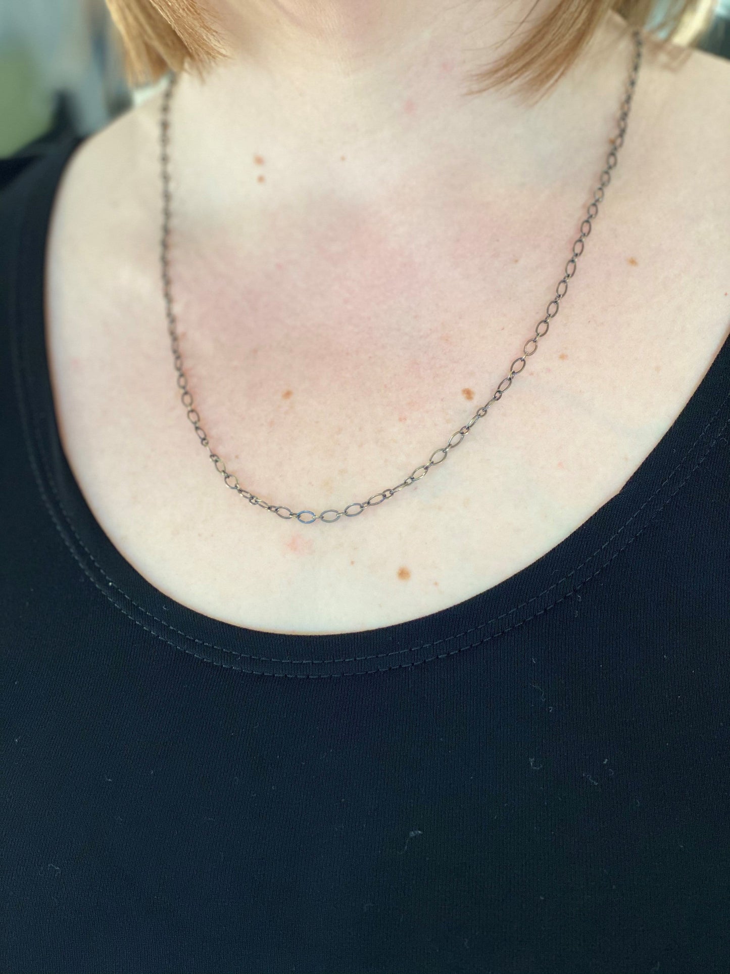 A person wearing a thin metal chain necklace over a black shirt, complete with a subtle chain extender for the perfect fit.