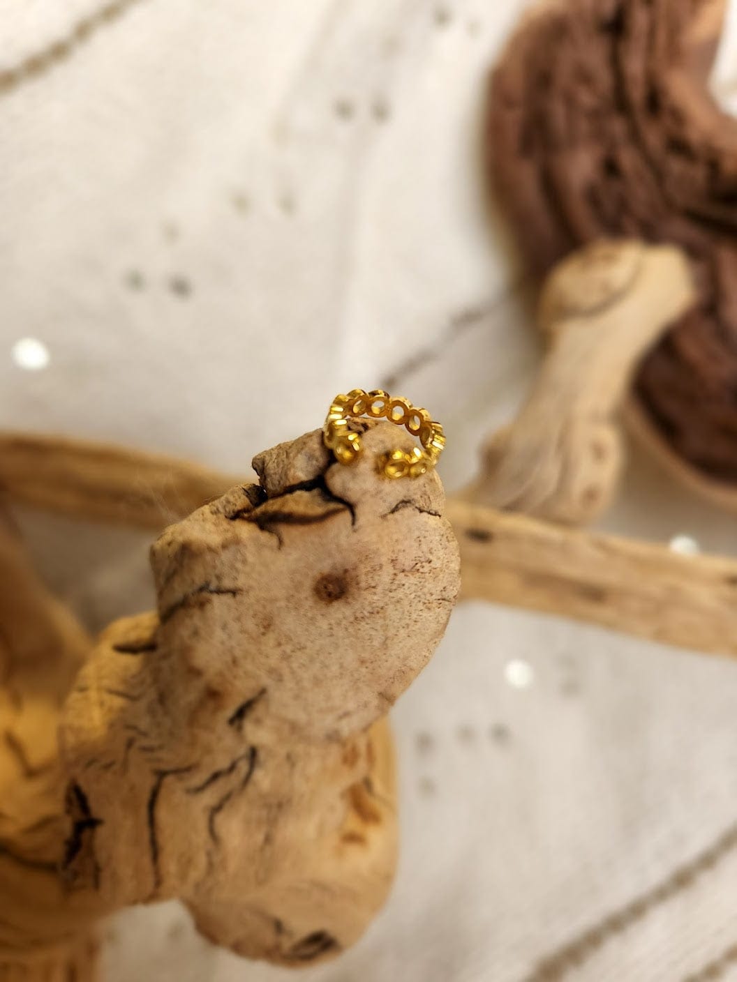 An 18K gold-plated ring with a braided design elegantly rests on driftwood, set against a textured background.