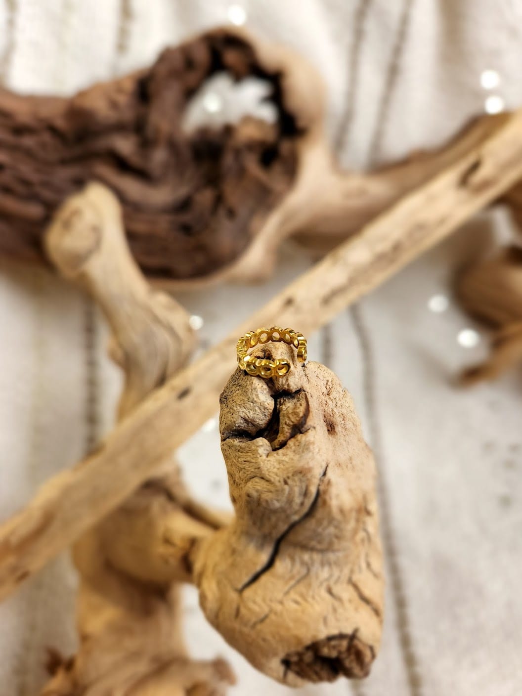 An exquisite beaded ring with hypoallergenic properties is elegantly displayed on a piece of driftwood against a neutral fabric background.
