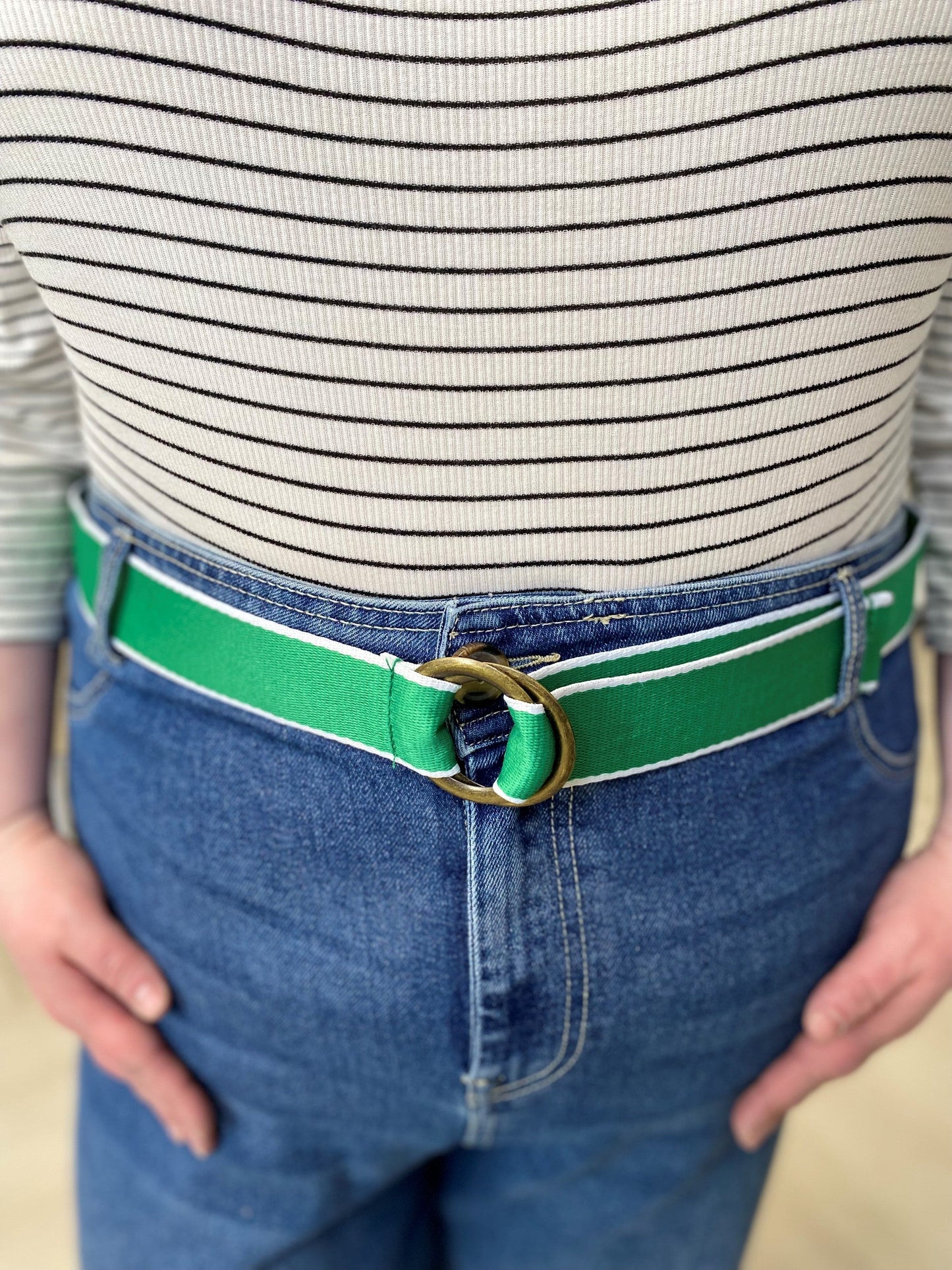 A person is wearing a striped shirt, blue jeans, and a rustic charm accessory—a bright green belt with a round buckle.