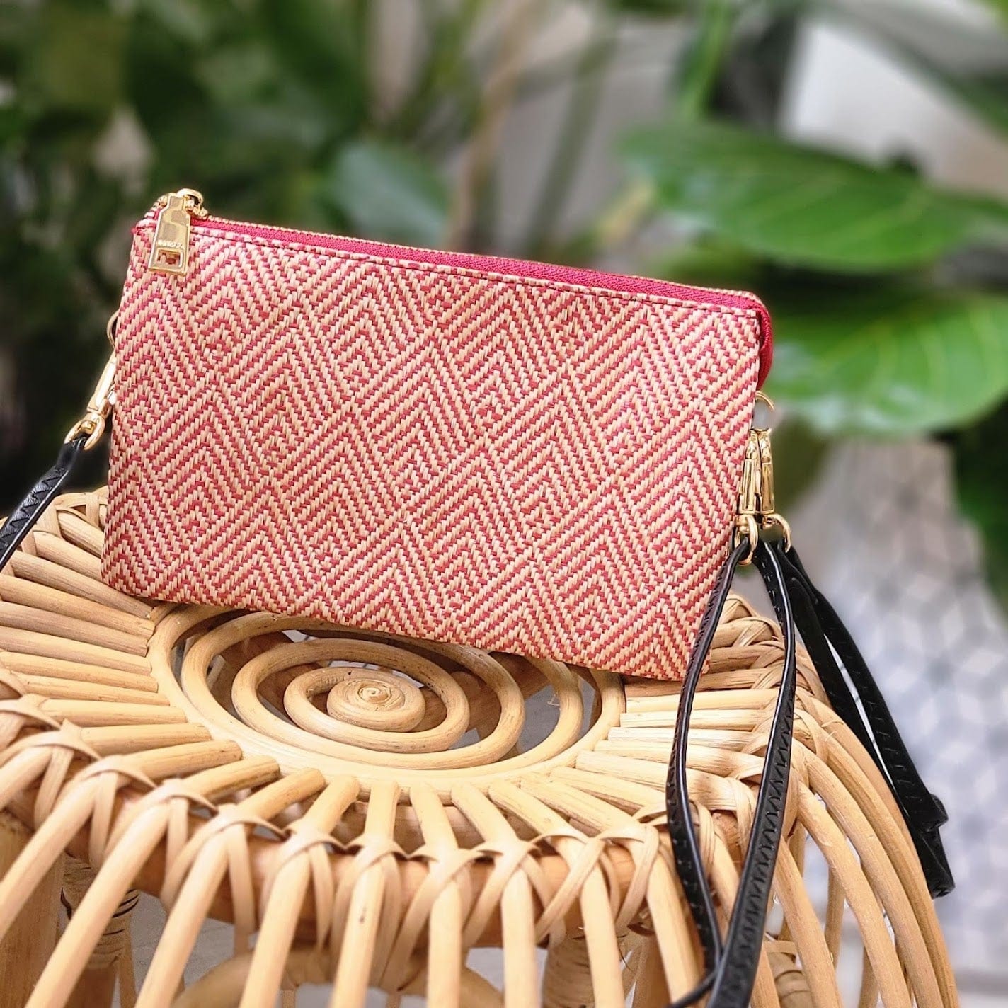 A pink and white woven clutch with gold hardware and a detachable faux leather strap elegantly rests on a wicker chair.
