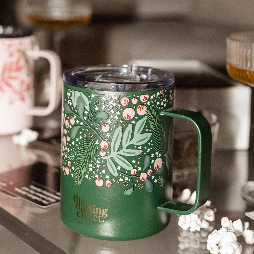 Green mug with floral design and the text "the darling effect" on a table, surrounded by popcorn and another triple-walled insulated mug in the background.