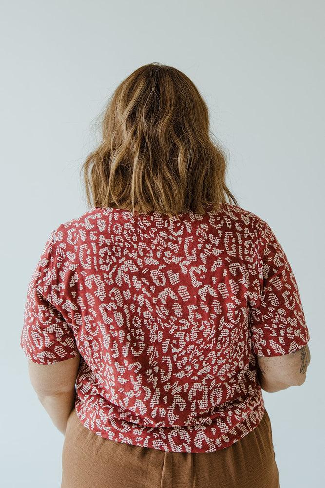 Person with shoulder-length hair, wearing a Love Marlow ABSTRACT ANIMAL PRINT SHORT SLEEVE TEE and brown pants, seen from behind against a plain background.