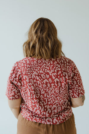 Person with shoulder-length hair, wearing a Love Marlow ABSTRACT ANIMAL PRINT SHORT SLEEVE TEE and brown pants, seen from behind against a plain background.