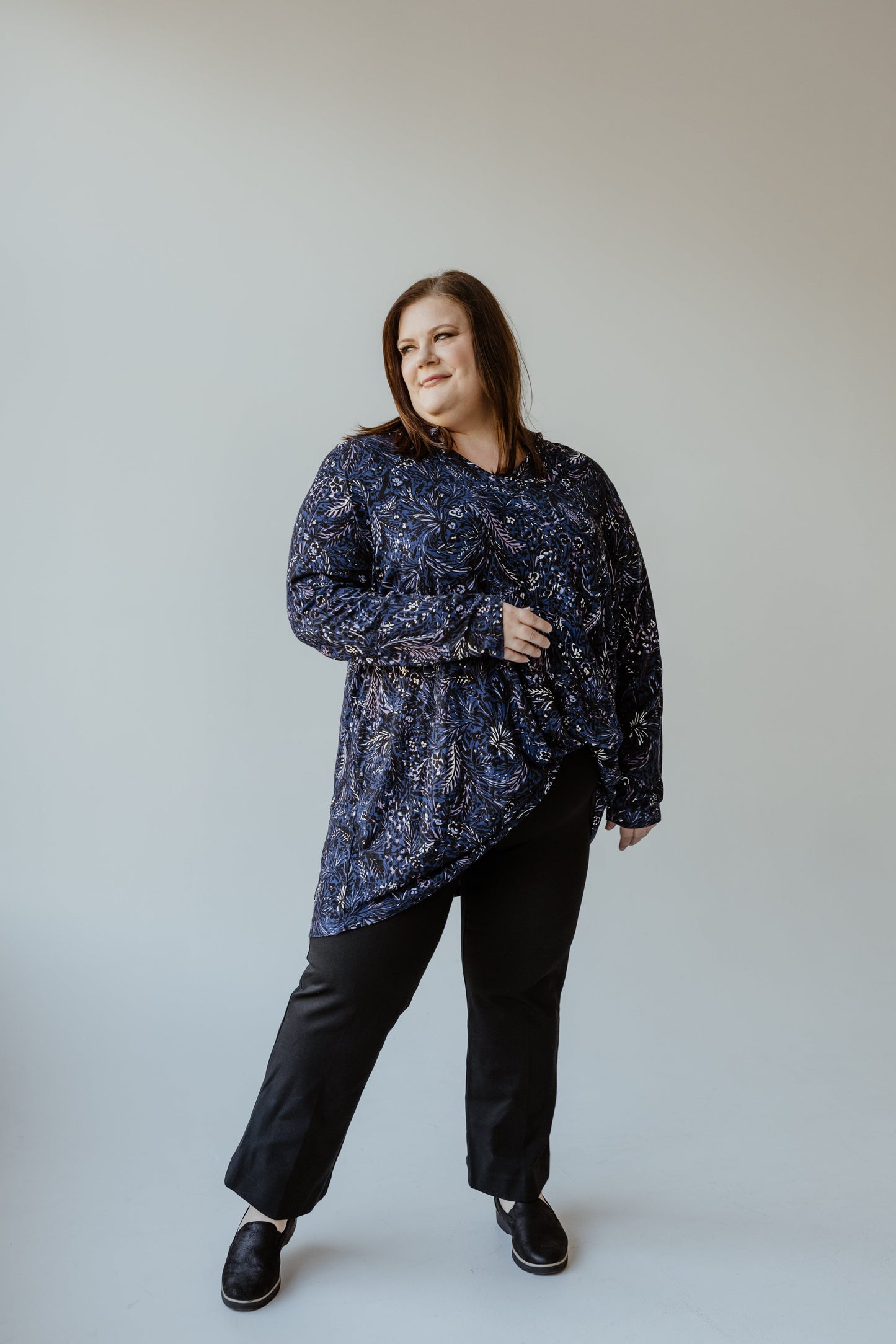 In a studio with a plain light background, a person is wearing the Yesta ABSTRACT FLORAL TURTLENECK BLOUSE and black pants.