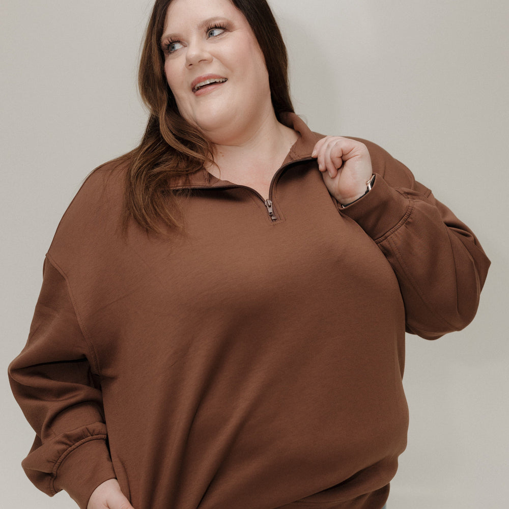 Woman wearing a brown sweater and blue jeans against a plain background
