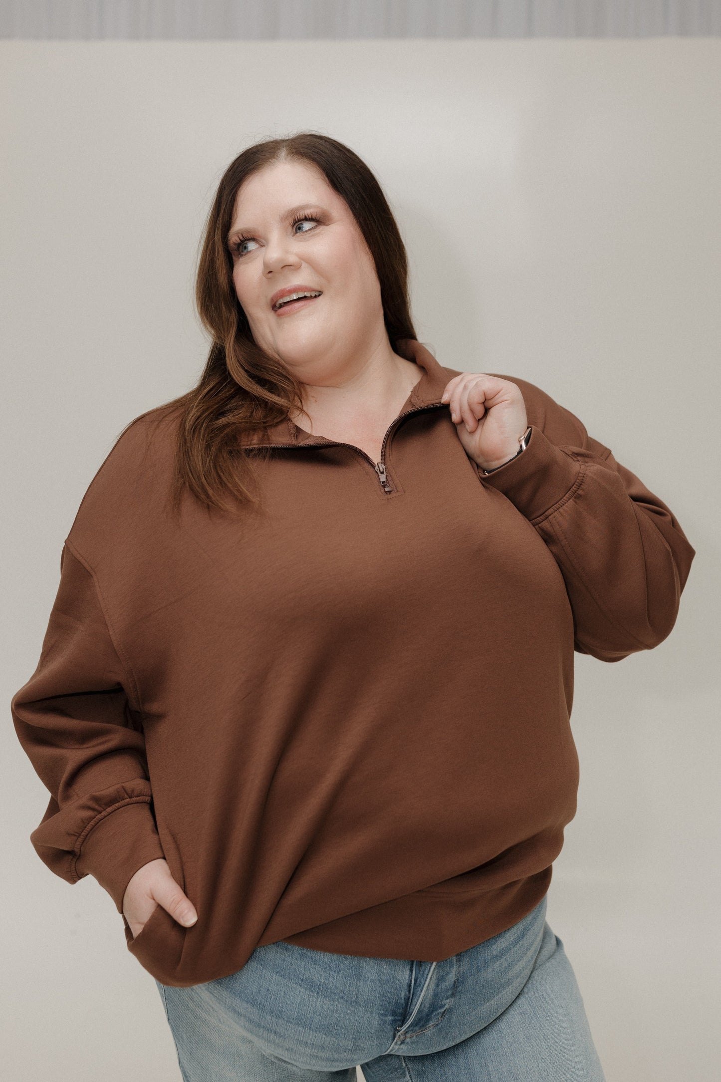 Woman wearing a brown sweater and blue jeans against a plain background