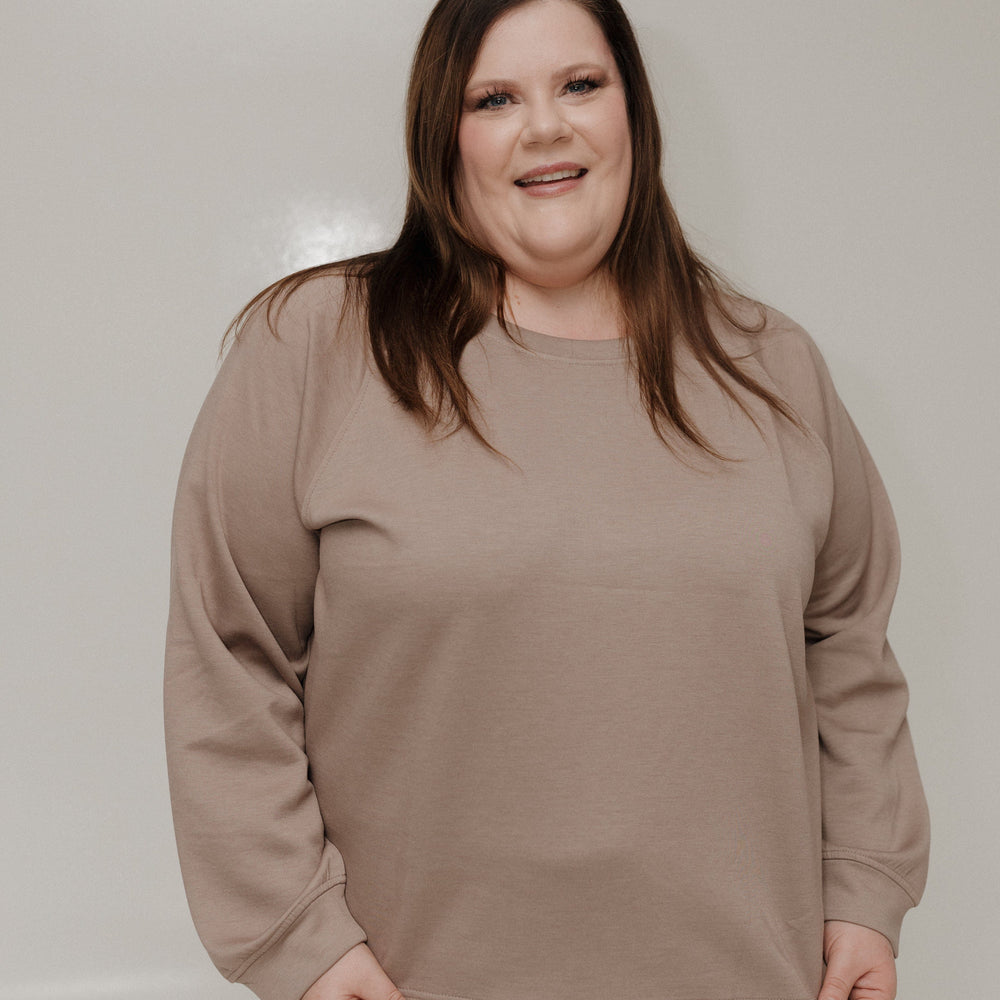 Woman wearing a beige sweatshirt and pants against a plain background