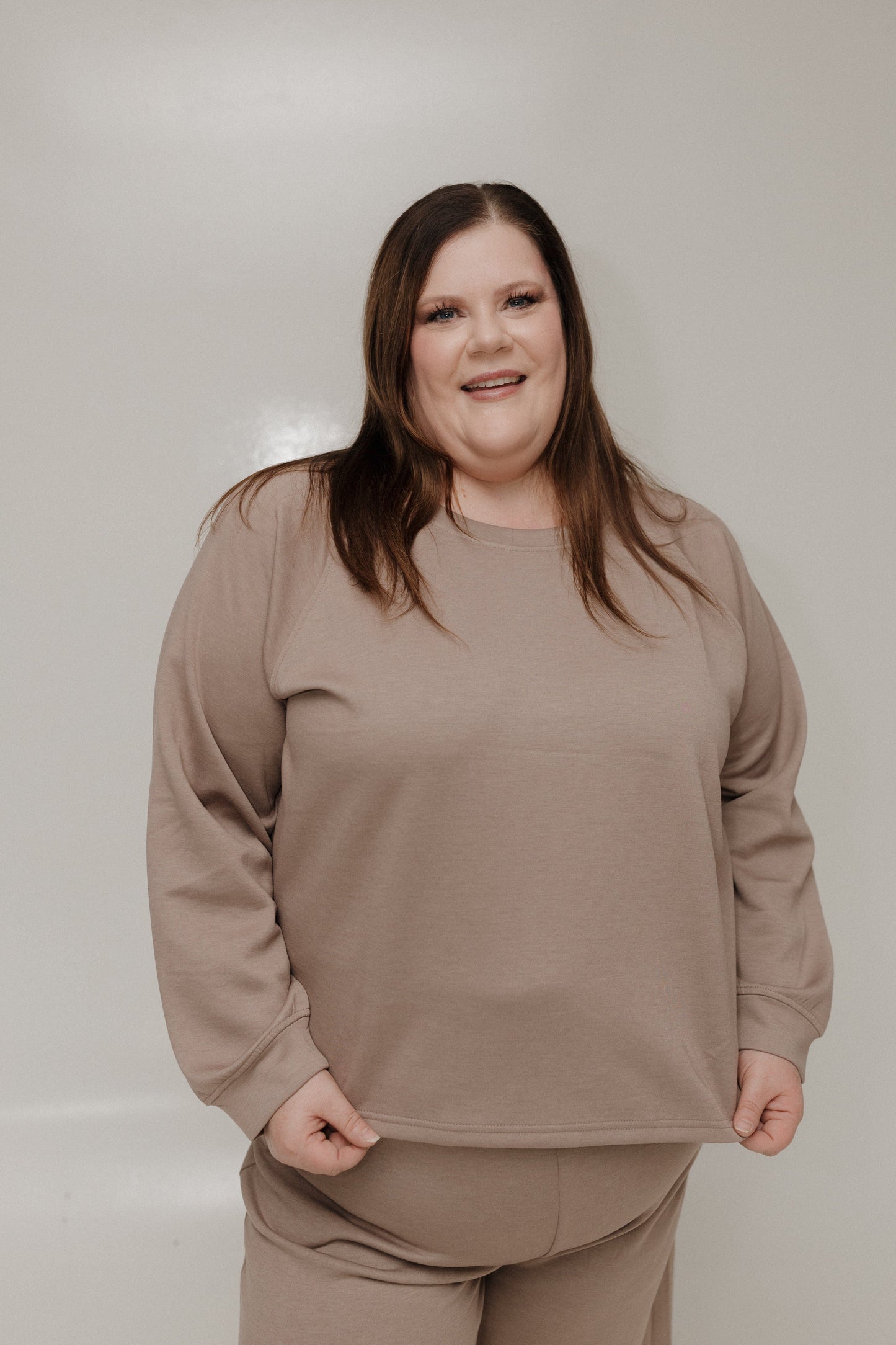 Woman wearing a beige sweatshirt and pants against a plain background