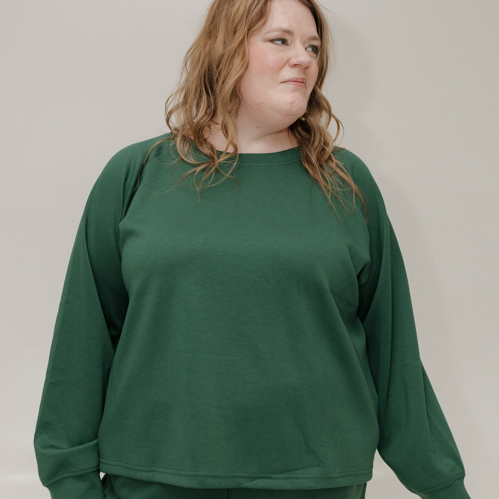 Person wearing a green sweatshirt and pants against a plain background