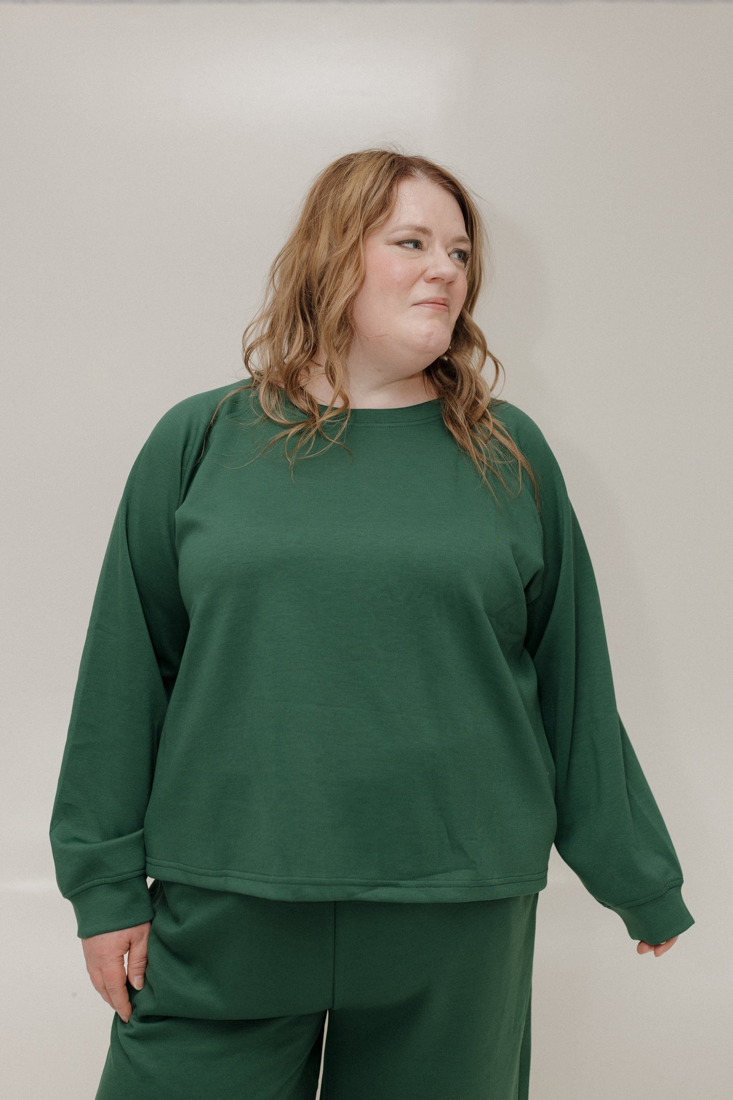 Person wearing a green sweatshirt and pants against a plain background