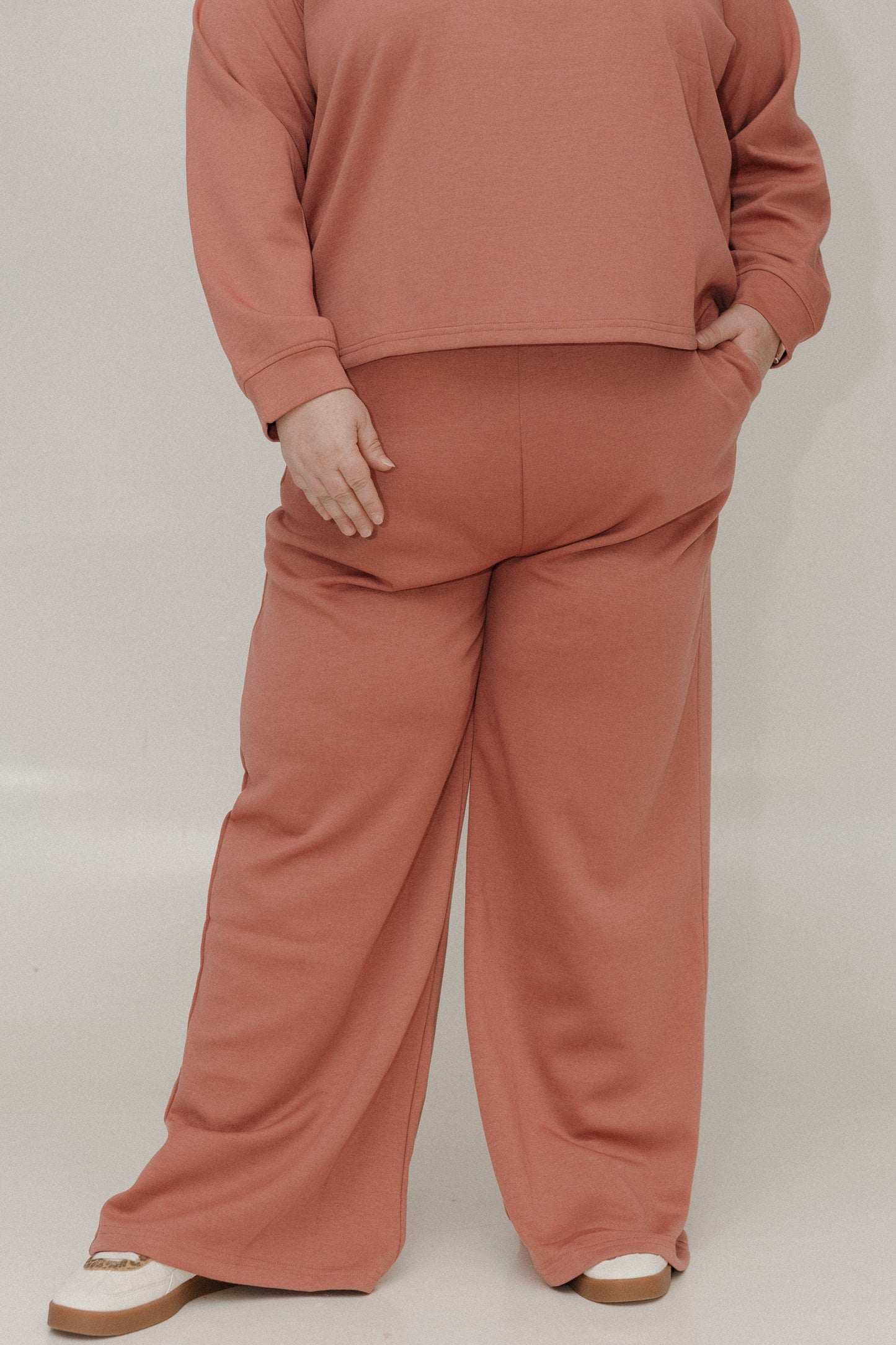 Person wearing a matching pink sweatshirt and pants set on a plain background