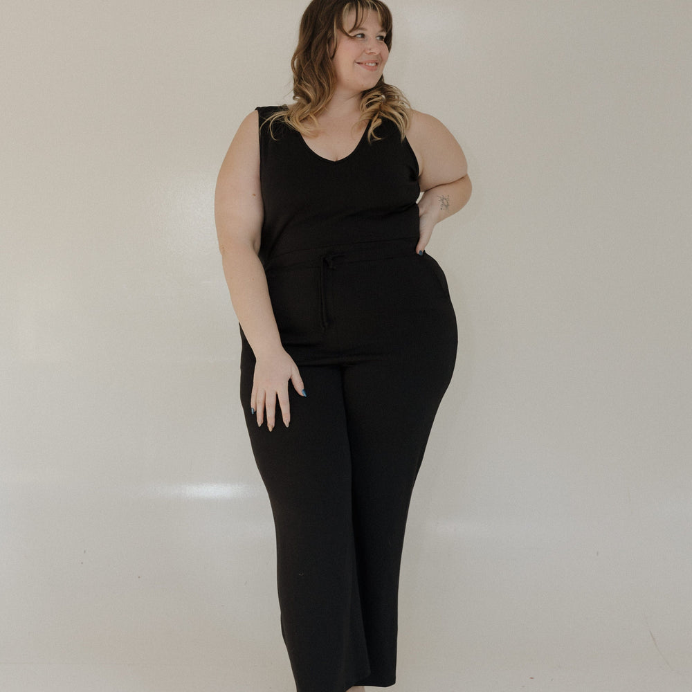 Woman wearing a black sleeveless jumpsuit against a plain background