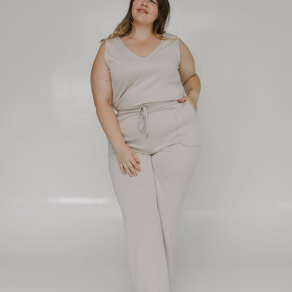 Woman wearing a beige sleeveless top and pants against a white background