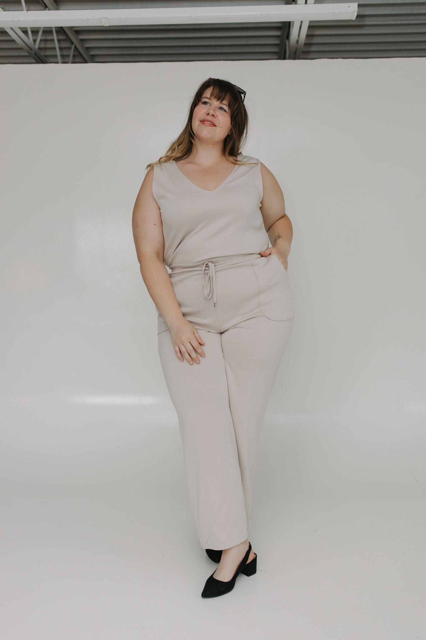 Woman wearing a beige sleeveless top and pants against a white background