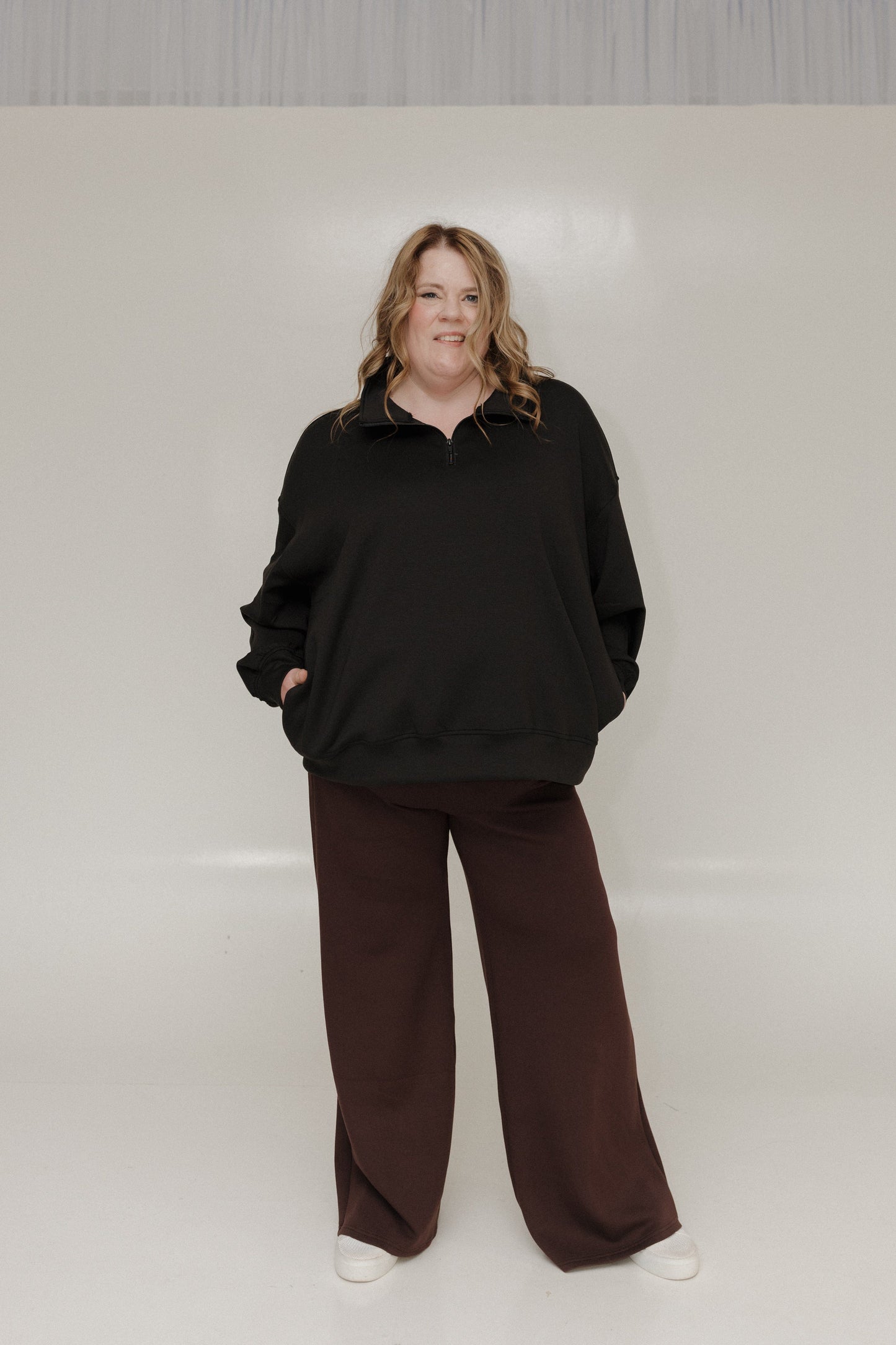 Person wearing a black sweater and brown pants against a white background