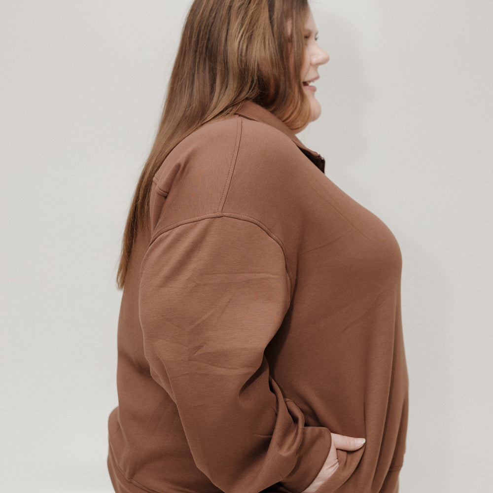Woman wearing a brown jacket and light blue jeans against a white background