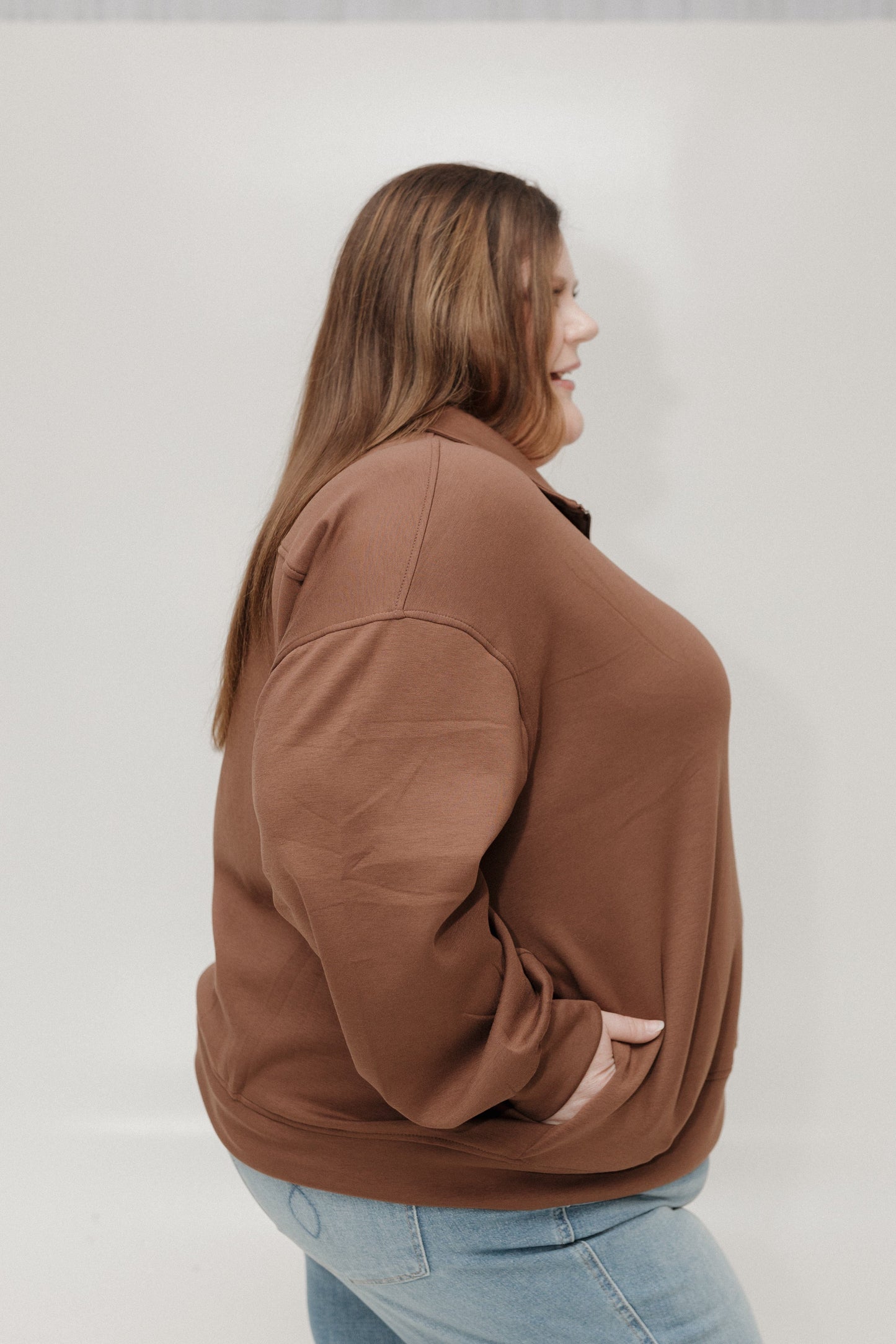 Woman wearing a brown jacket and light blue jeans against a white background