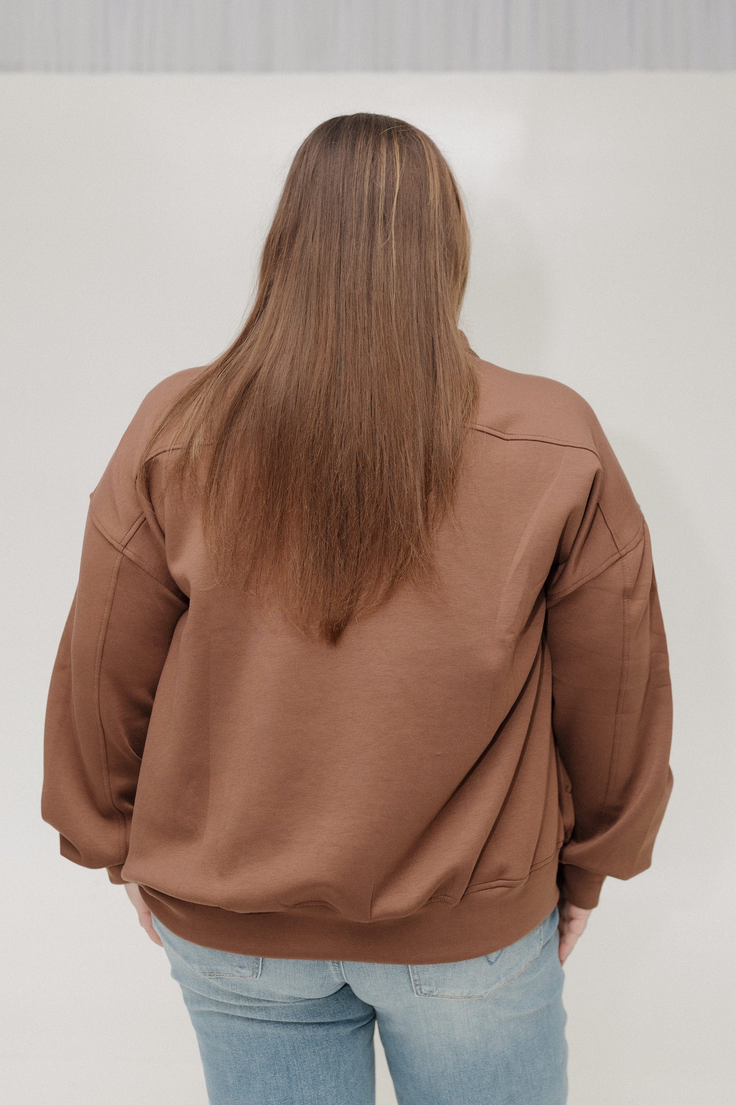 Person wearing a brown jacket and light blue jeans against a white background