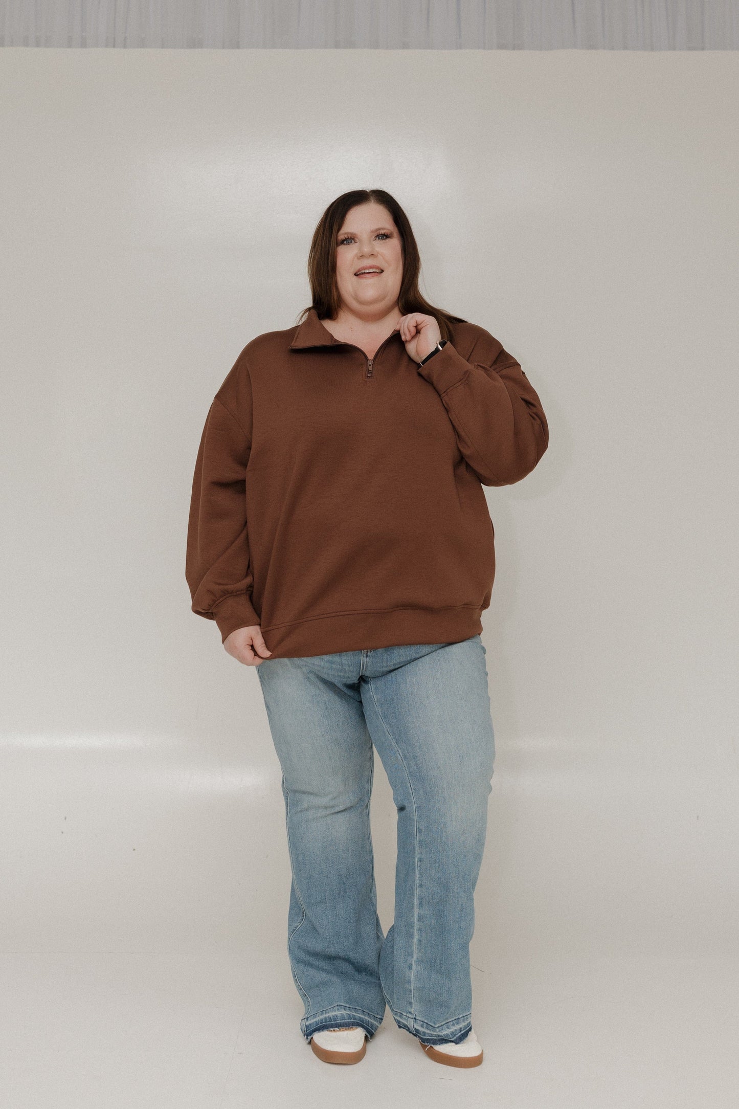 Person wearing a brown sweater and blue jeans against a plain background