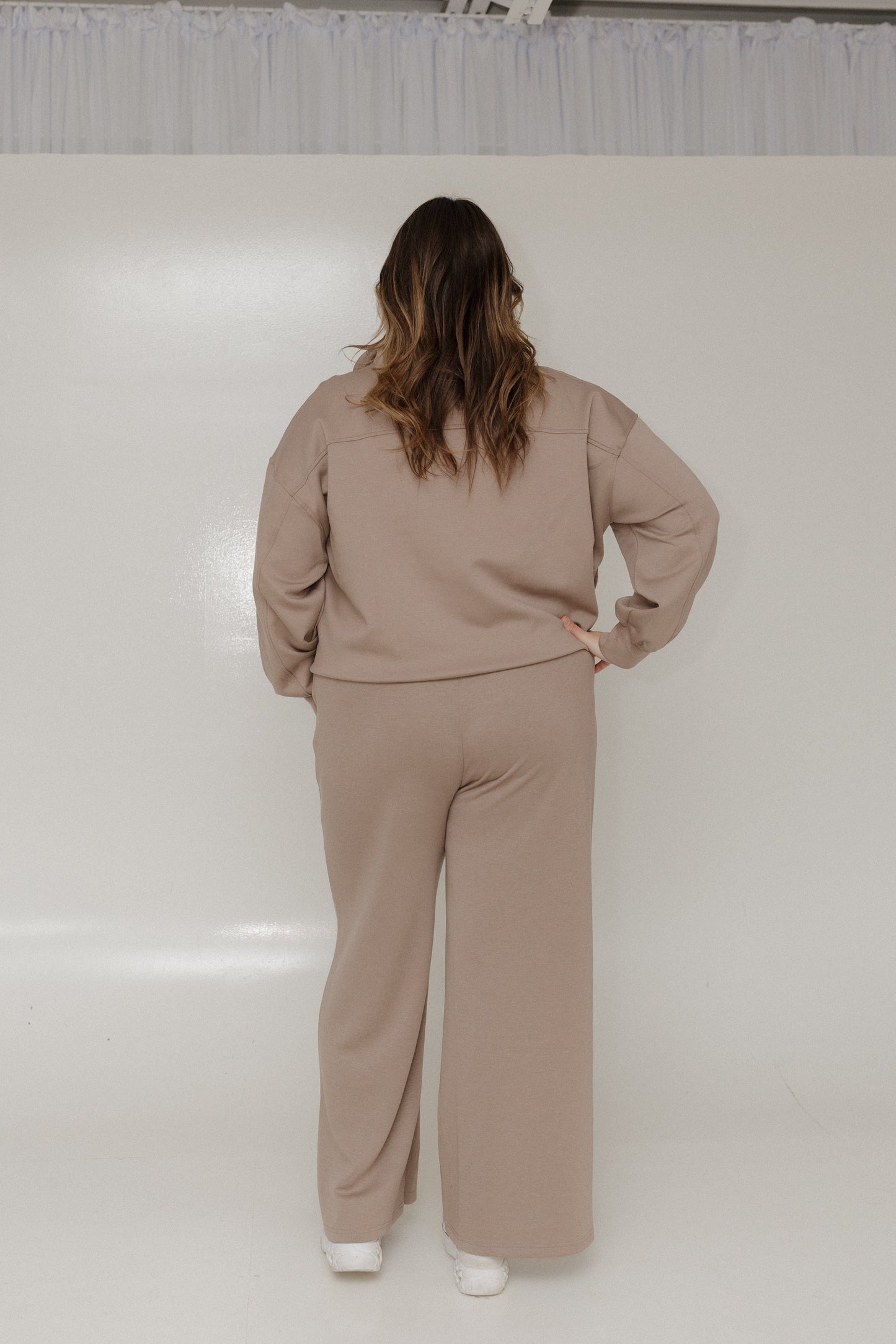 Person wearing a beige tracksuit standing against a white wall