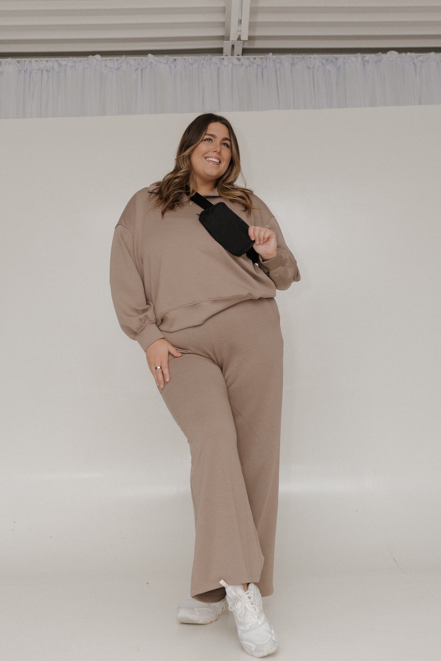 Woman wearing a beige outfit with a black top against a white background