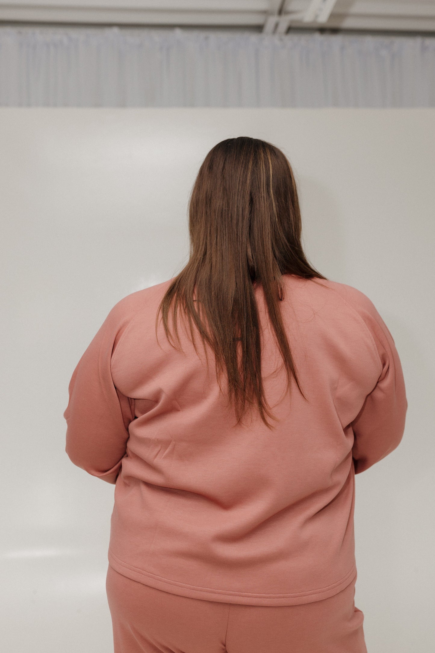 Person wearing a pink outfit standing against a white wall