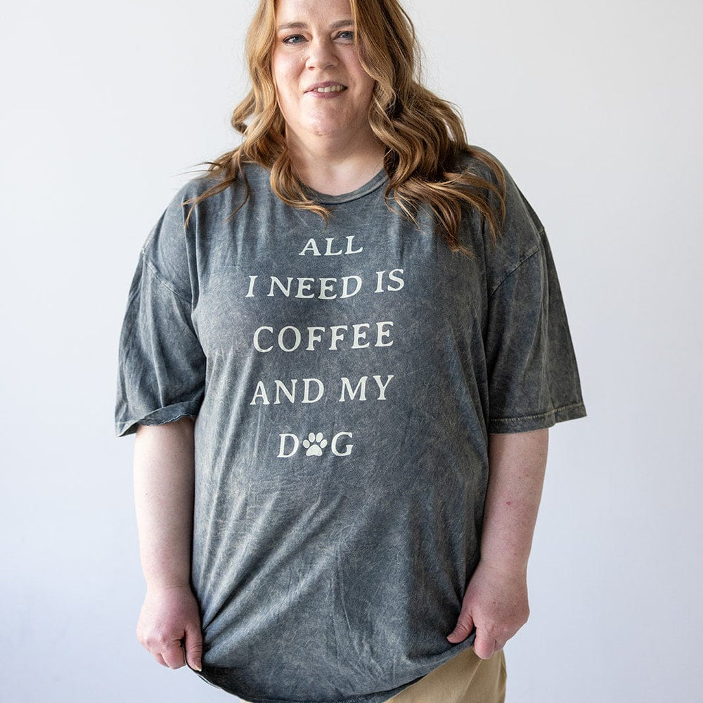 A person in a casual outfit sports a gray graphic tee emblazoned with "All I need is coffee and my dog.