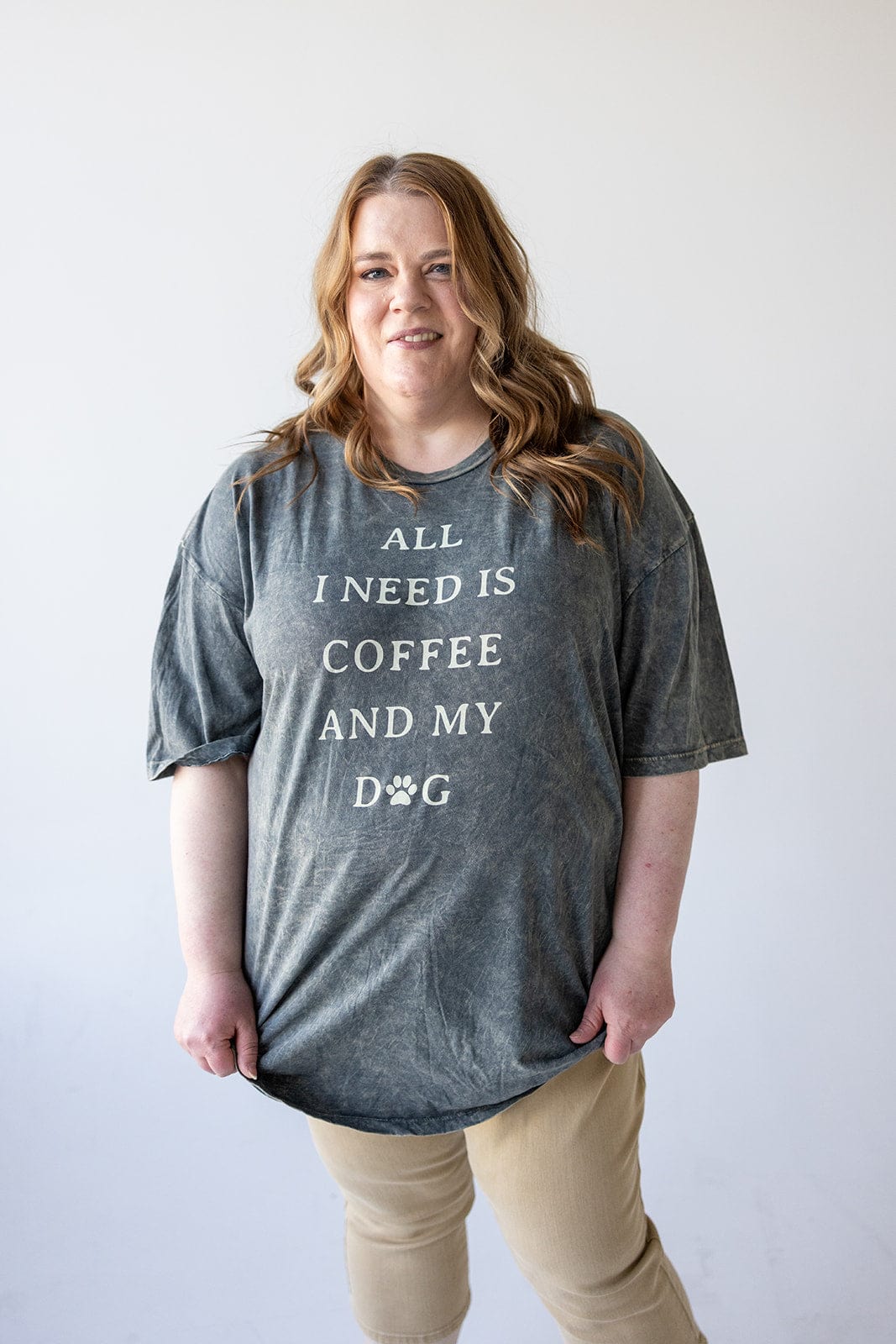 A person in a casual outfit sports a gray graphic tee emblazoned with "All I need is coffee and my dog.