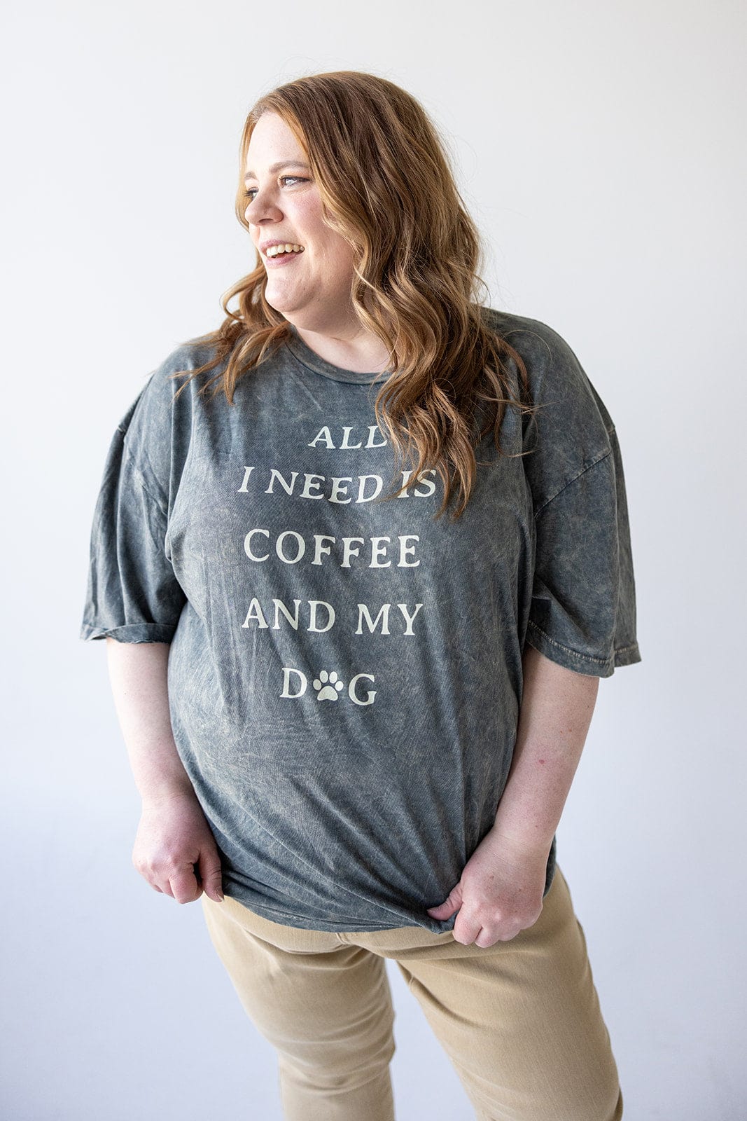 A person in a graphic tee that reads "ALL I NEED IS COFFEE AND MY DOG" is smiling and gazing to the side, perfectly embodying a casual outfit vibe.