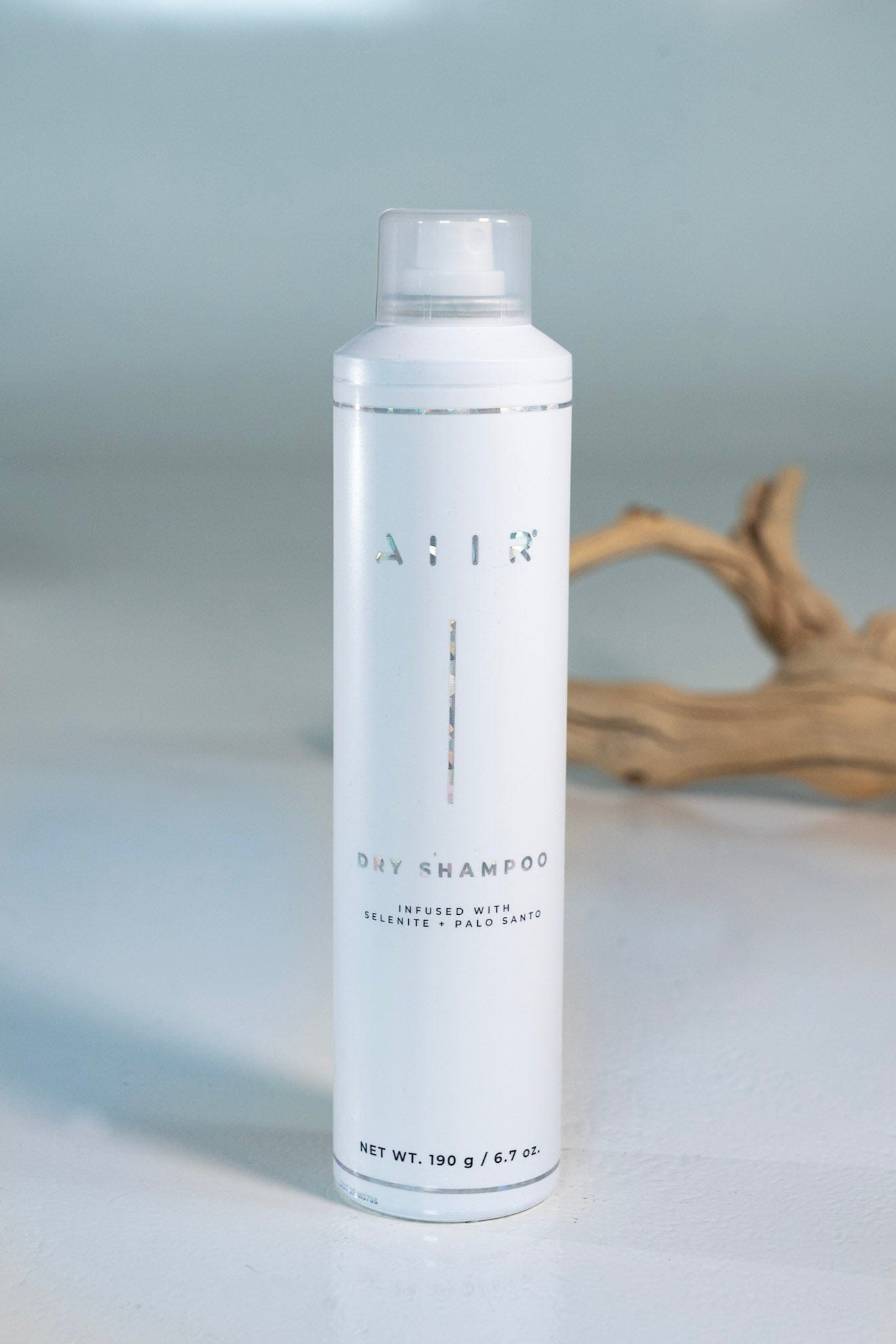 White bottle of AIIR dry shampoo on a light gray background