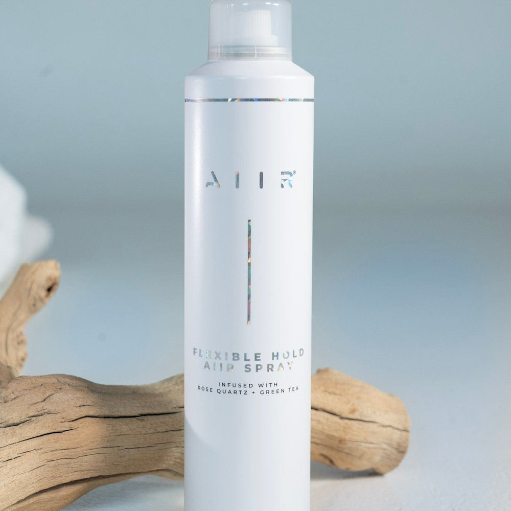 White hair spray bottle labeled 'AIR' on a light gray background with wooden driftwood.