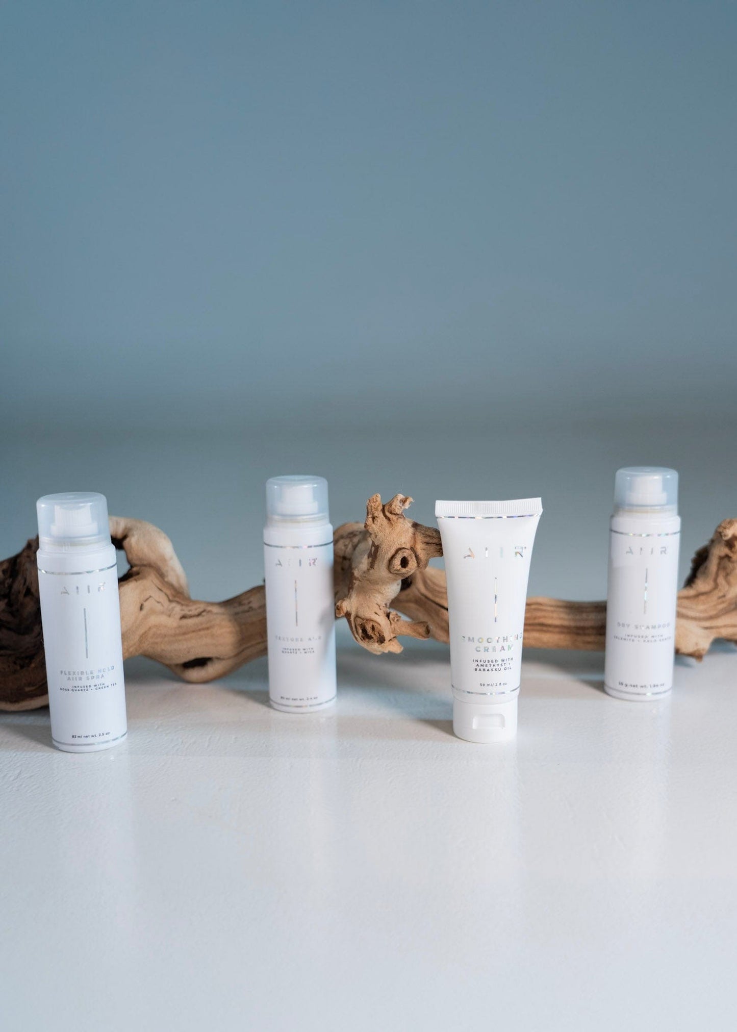 Four skincare bottles with labels on a light surface with driftwood.