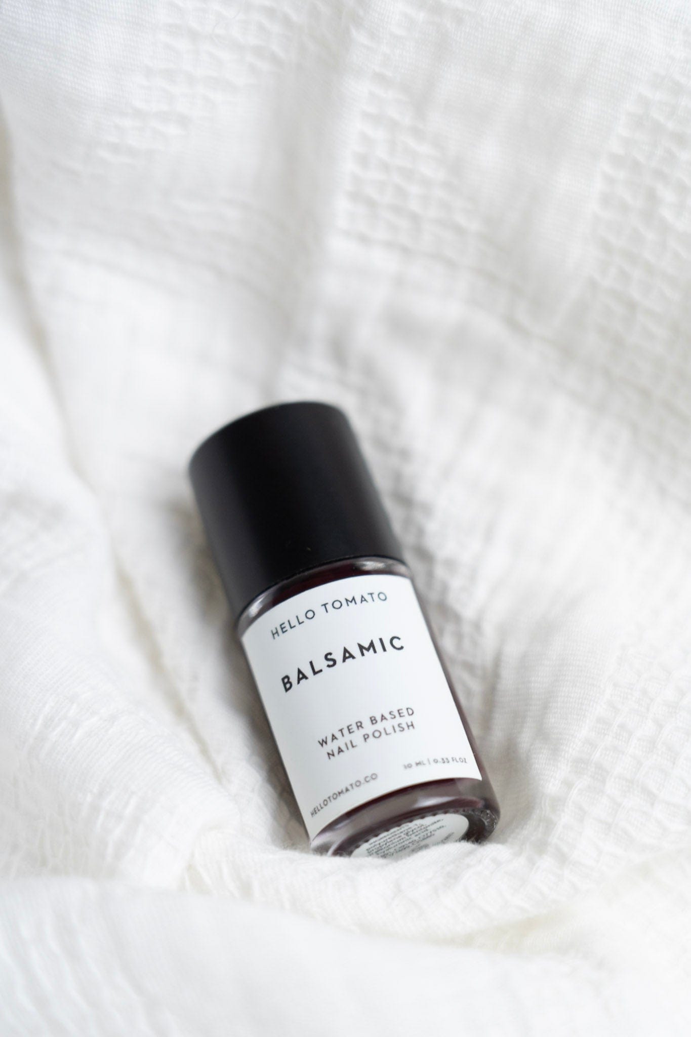 Balsamic water-based nail polish bottle on a white textured background