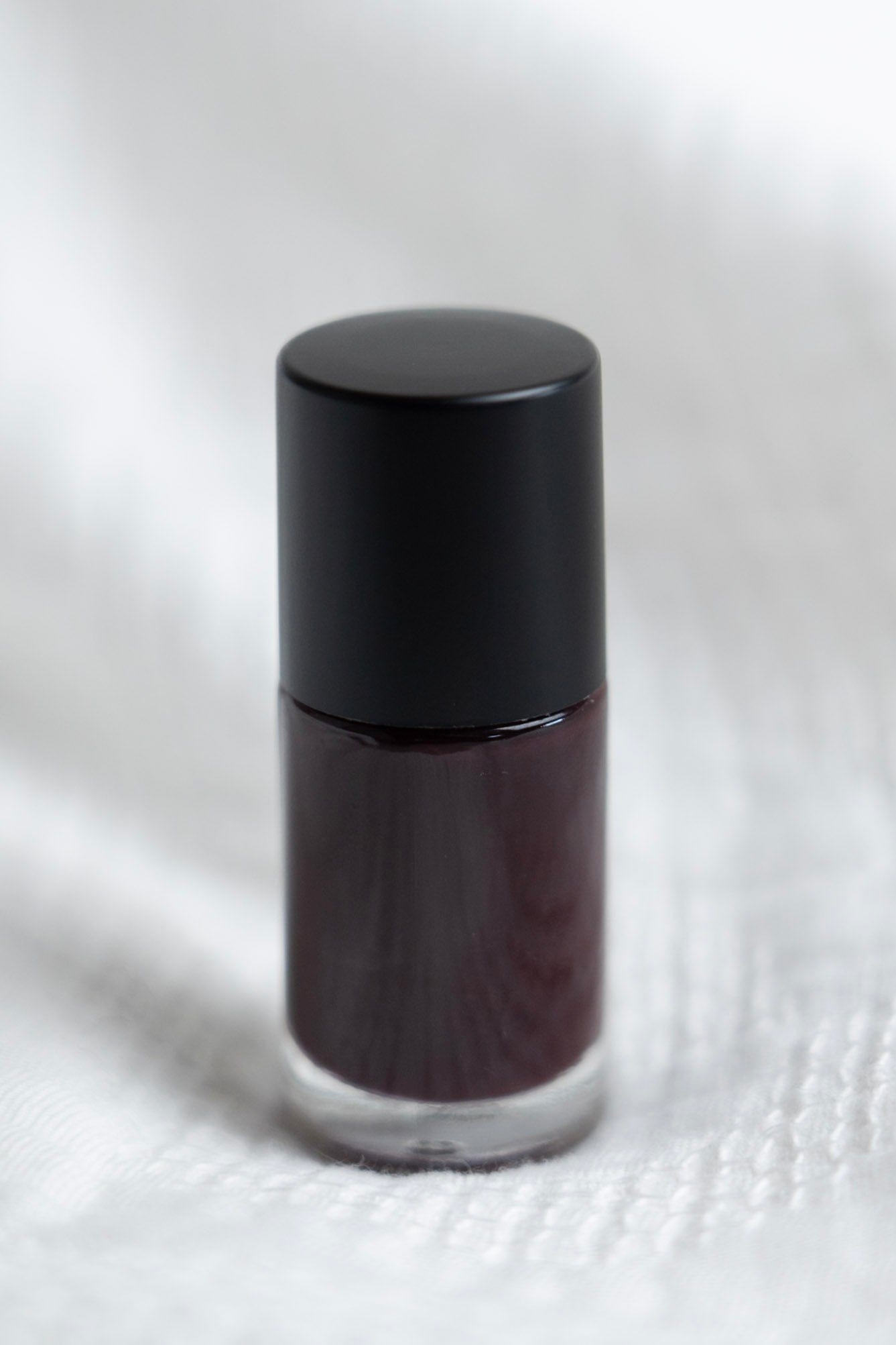 Balsamic water-based nail polish bottle on a white textured background textured white surface