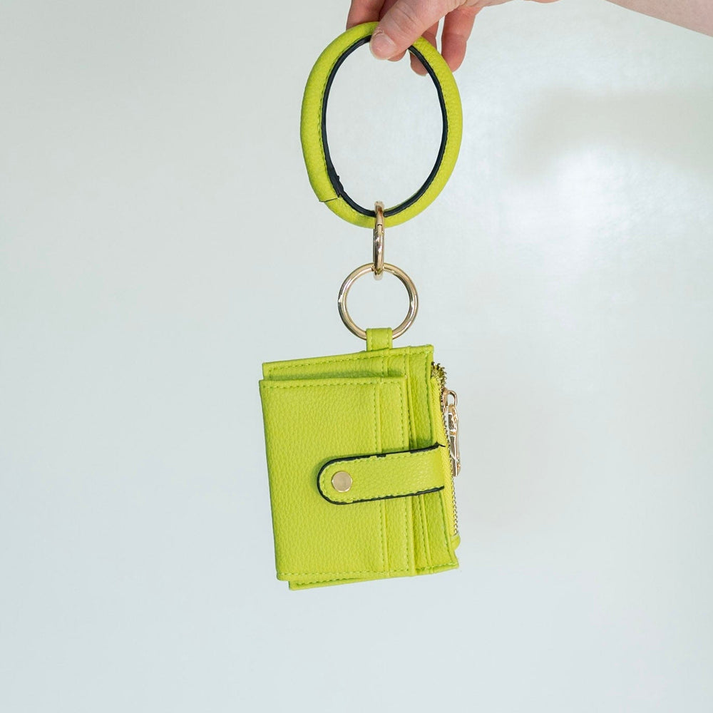 No need to grab your entire purse with this little wallet! The cute bangle detail adds style and helps you not lose it! Unsnap the clasp, and it unfolds to reveal the billfold! It has a zipper change pocket and inside card and ID slots. This gorgeous, fun pop of color in this avocado green will make any outfit stand out! Dimension: 5” Long x 4” High
