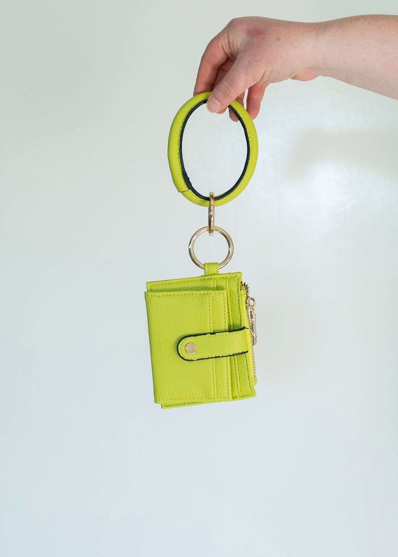 No need to grab your entire purse with this little wallet! The cute bangle detail adds style and helps you not lose it! Unsnap the clasp, and it unfolds to reveal the billfold! It has a zipper change pocket and inside card and ID slots. This gorgeous, fun pop of color in this avocado green will make any outfit stand out! Dimension: 5” Long x 4” High