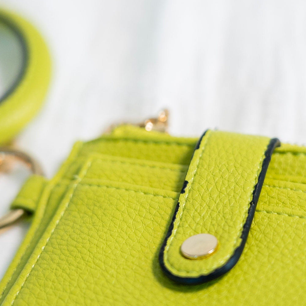 No need to grab your entire purse with this little wallet! The cute bangle detail adds style and helps you not lose it! Unsnap the clasp, and it unfolds to reveal the billfold! It has a zipper change pocket and inside card and ID slots. This gorgeous, fun pop of color in this avocado green will make any outfit stand out! Dimension: 5” Long x 4” High