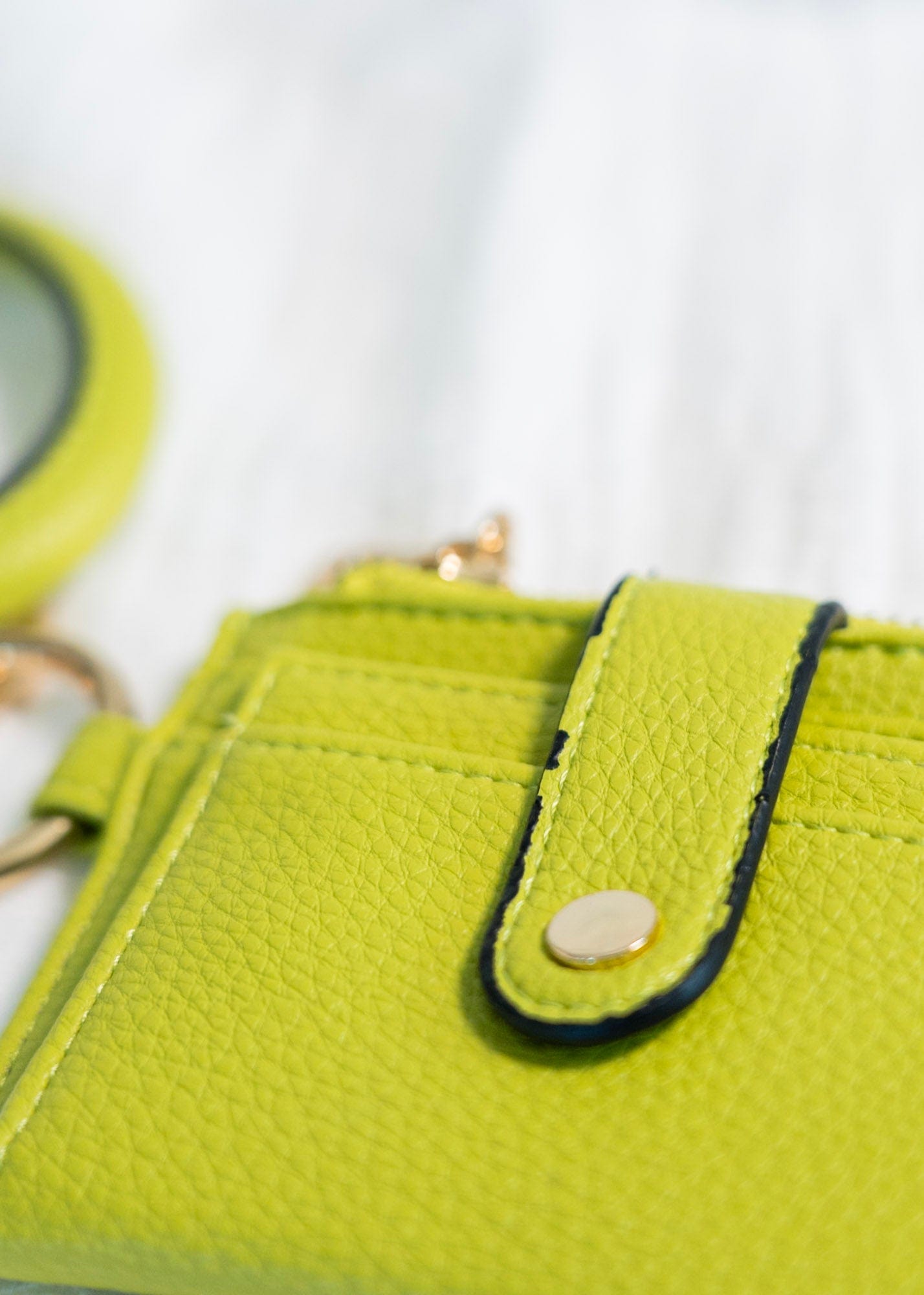 No need to grab your entire purse with this little wallet! The cute bangle detail adds style and helps you not lose it! Unsnap the clasp, and it unfolds to reveal the billfold! It has a zipper change pocket and inside card and ID slots. This gorgeous, fun pop of color in this avocado green will make any outfit stand out! Dimension: 5” Long x 4” High