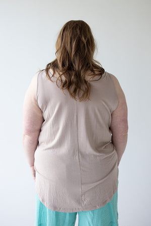 Person with long brown hair wearing a chic and comfy BASIC ROUND NECK TUNIC TANK IN FROSTED TOFFEE by Love Marlow and light blue pants, seen from behind against a plain white background.