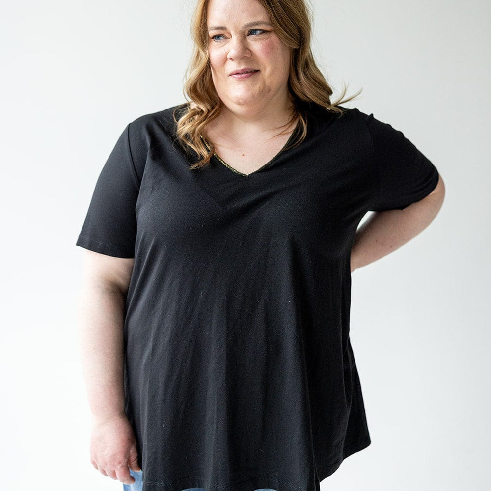 A person with long hair, wearing Love Marlow's BASIC V-NECK TEE WITH BRONZE SPARKLE IN BLACK and ripped jeans, stands against a plain white background.