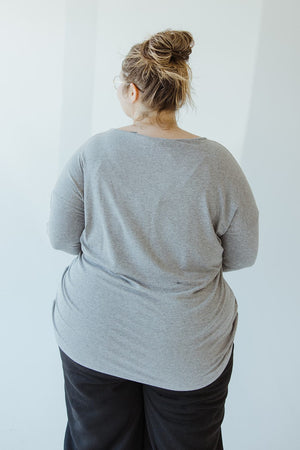 A person with their back to the camera, wearing black pants and a Yesta BASIC DOLMAN TUNIC in HEATHER GREY. Their hair is tied up in a messy bun.