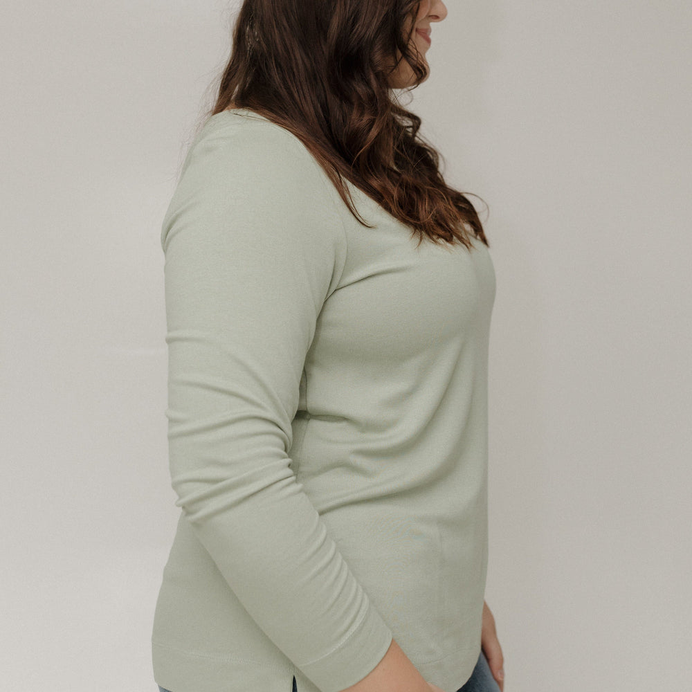 Person wearing a light green long-sleeve top and blue jeans against a plain background