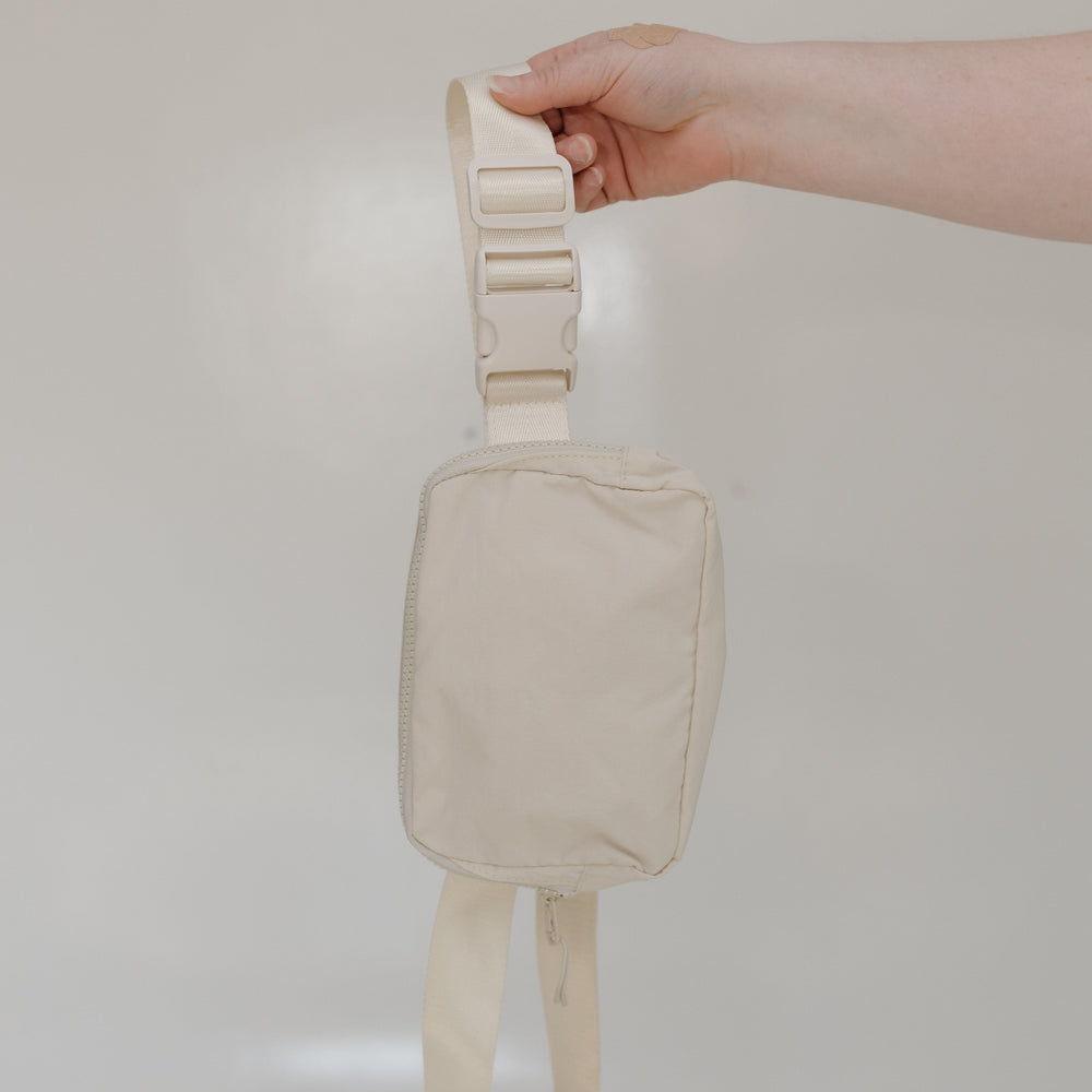 Beige strap bag held by a hand against a plain background