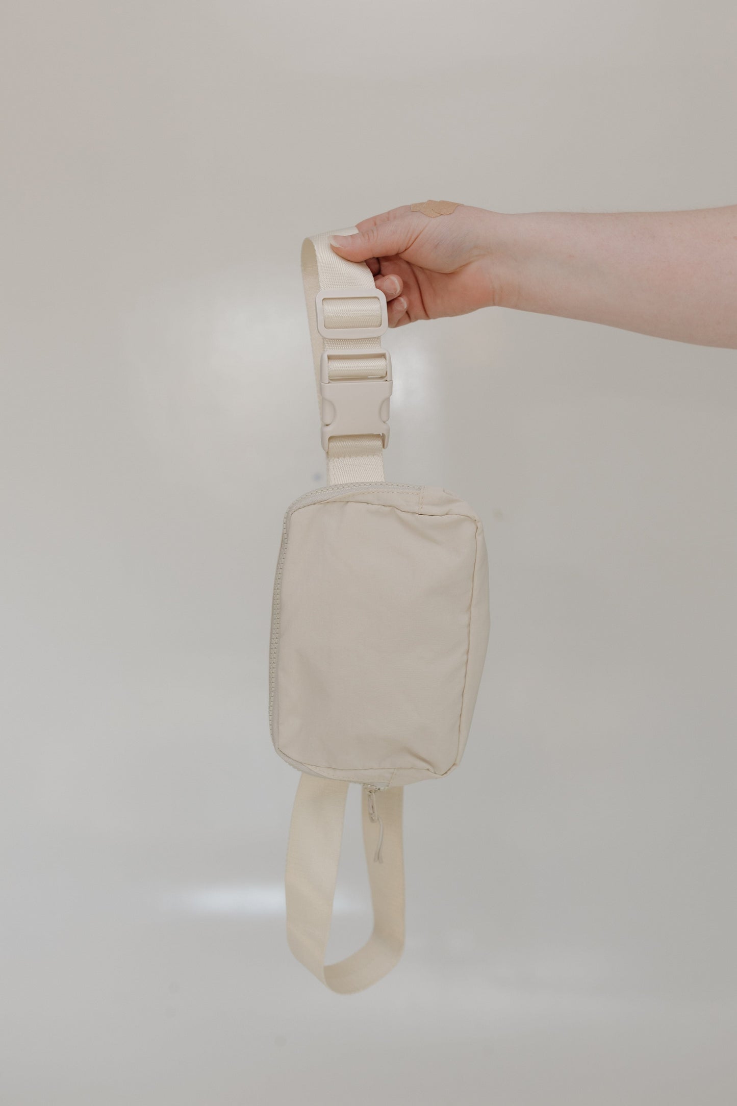 Beige strap bag held by a hand against a plain background