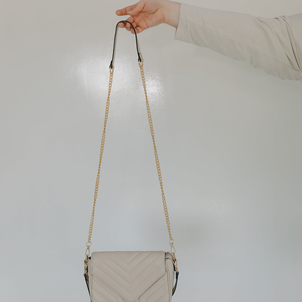 Beige handbag with a chain strap held by a hand against a light background